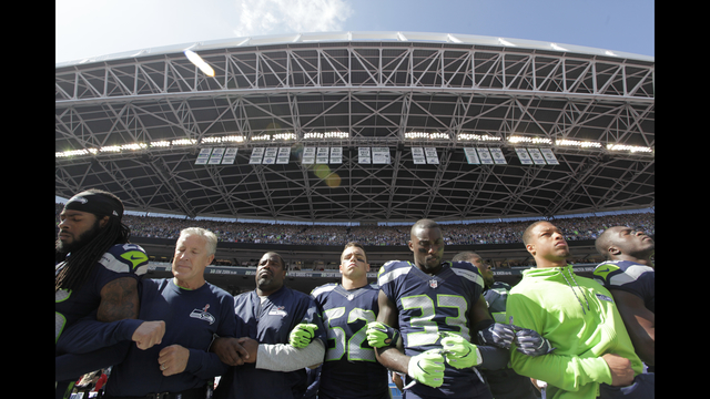 Seattle Seahawks players and coaches including cornerback Richard Sherman and head coach Pete Carroll second from left stand and link arms during the singing of the national anthem before an NFL football game against the Miami Dolphins Sunday Se