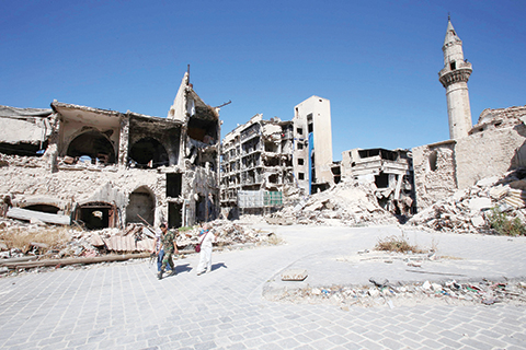 A Syrian government soldier and unidentified people walk in the damaged Khan al Wazir market in the government-held side of Aleppo's historic city centre