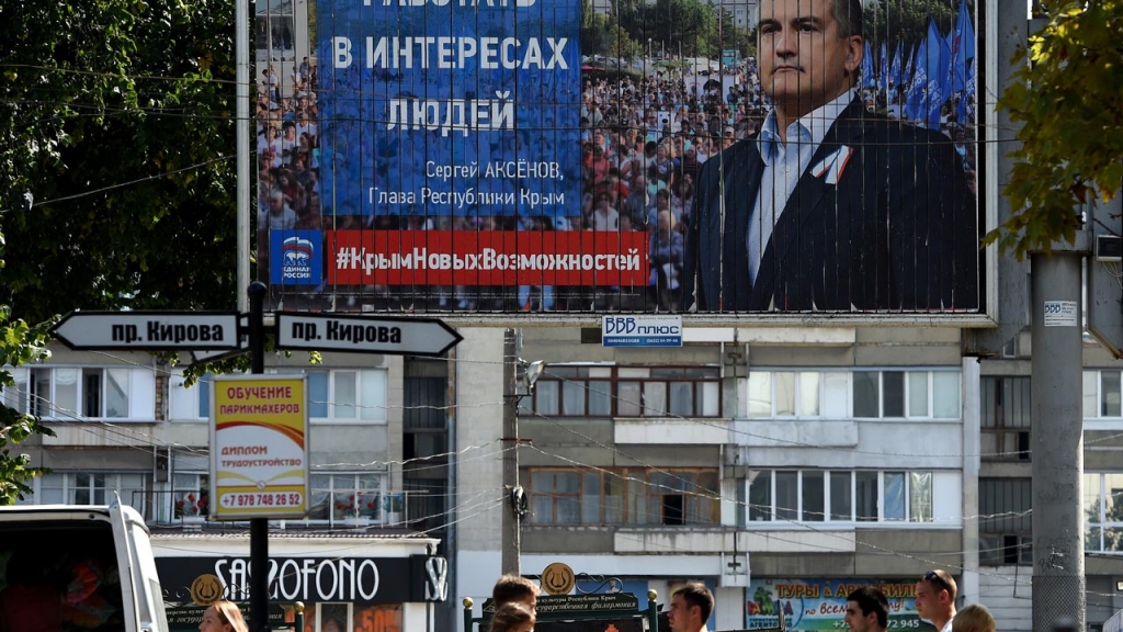 10 2016 in the main Crimean city of Simferopol shows people walking next to an election billboard for the United Russia party with a portrait of Crimean leader Sergei Aksyonov. Two-and-a-half years after Moscow annexed the