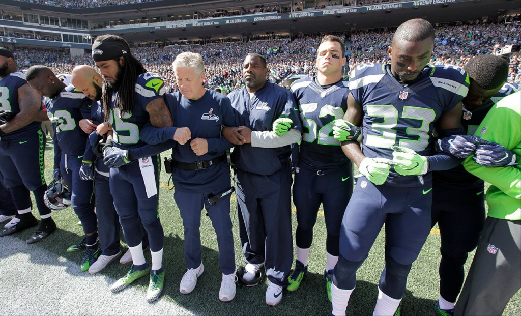 Seattle Seahawks players and coaches including head coach Pete Carroll center left stand and link arms during the singing of the national anthem before an NFL football game against the Miami Dolphins Sunday in Seattle