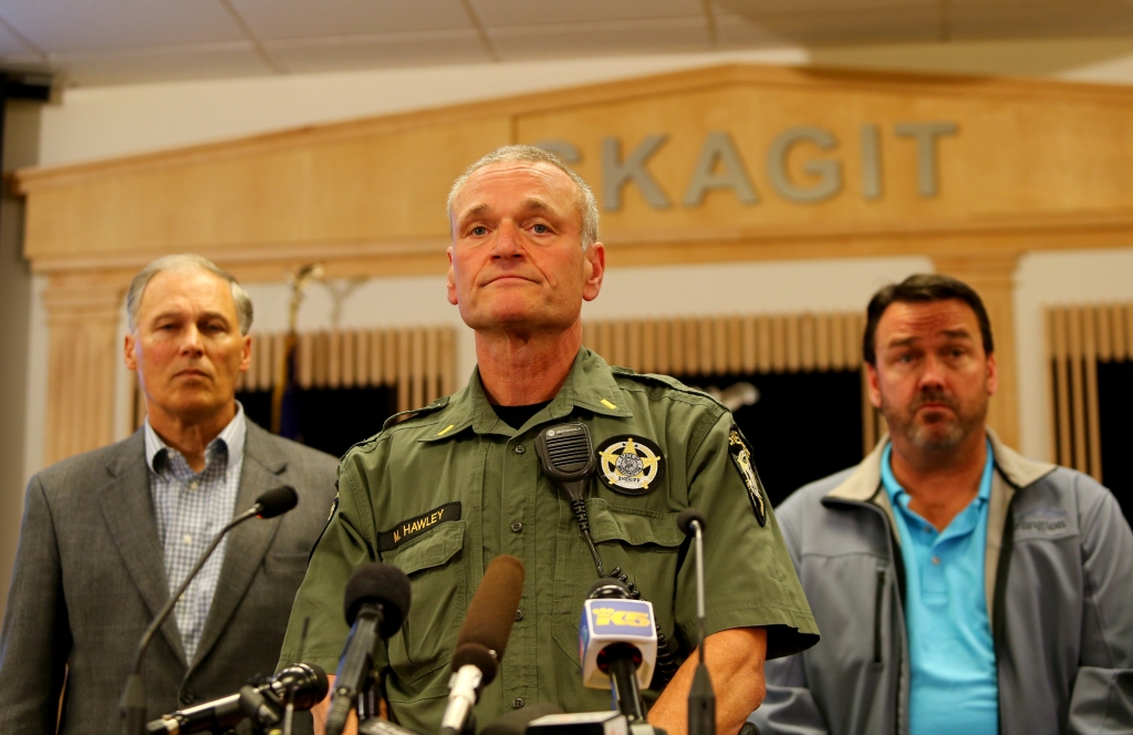 Governor Jay Inslee of Washington and Mayor Steve Sexton of Burlington listen as Washington state Patrol officer Keith Leary speaks at a press conference