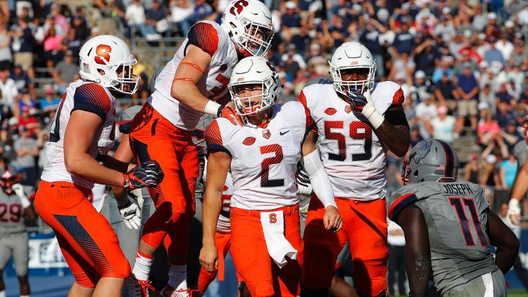 Syracuse quarterback Eric Dungey is congratulated by teammates as Connecticut linebacker Junior Joseph looks on after he scored the winning touchdown during the second half of Syracuse's 31-24 win over Connecticut at Rentschler Field. (Winsl