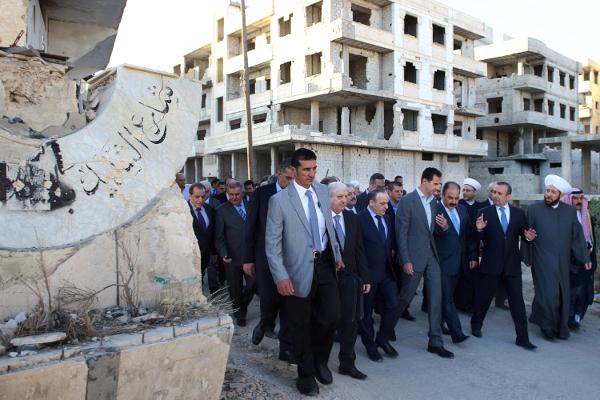 Syrian official news agency SANA Syrian President Bashar Assad walks on a street with officials after performing the morning Eid al Adha prayers in Daraya a blockaded Damascus suburb Syria Sept. 12 2016