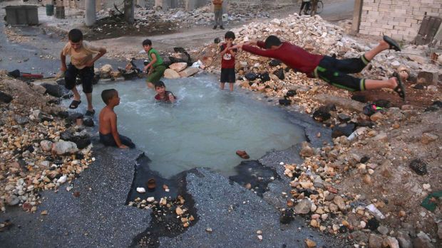 Syrian boys dive into a hole filled with water caused by a missile attack in Aleppo