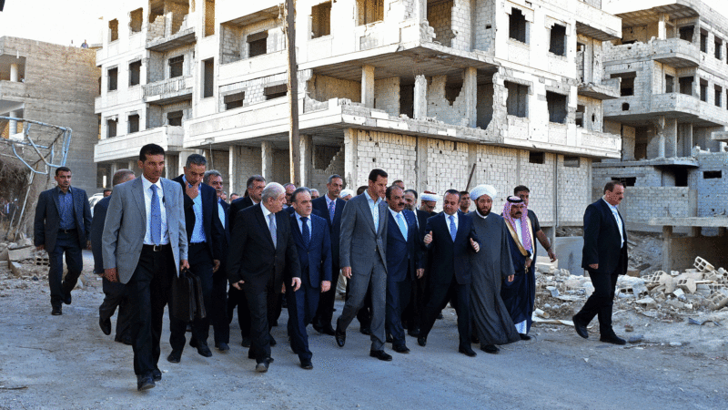 Syrian official news agency SANA Syrian President Bashar Assad center walks on a street with officials after performing the morning Eid al Adha prayers in Daraya a blockaded Damascus suburb Syria Monday Sept. 12 2016