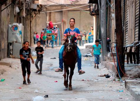 A Syrian boy rides a horse as Syrian children play in the street in the northern Syrian city of Aleppo as they celebrate the Eid al Adha holiday on the first day of a fragile ceasefire