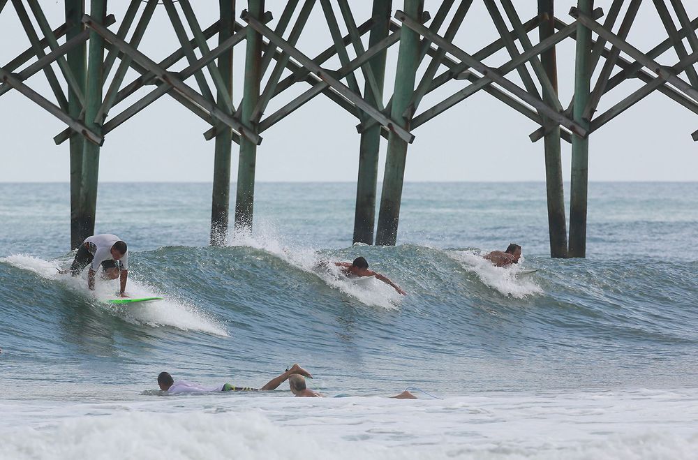 Surfers vie for a spot on a wave near the Surf City Pier Surf City N.C. Tuesday Aug. 30 2016 as incoming tide and light offshore winds create good surfing. Crowds thinned Tuesday on the beaches of North Carolina's Outer Banks ahead of a tropical wea