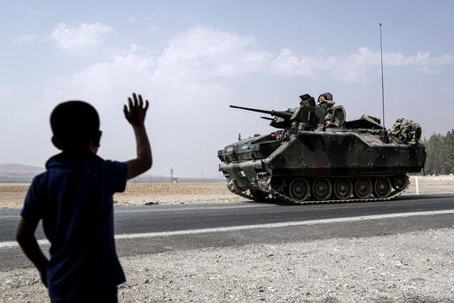 A child waves toward Turkish troops heading to the Syrian border in Karkamis Turkey Friday Aug. 26 2016. Turkey's state-run Anadolu news agency said late Thursday Turkish artillery have shelled a group of Syrian Kurdish militia fighters in the north