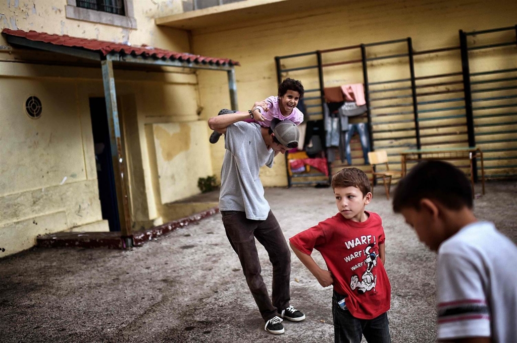 Image Children play at the yard of an abandoned school used by volunteers for hosting families of refugeees