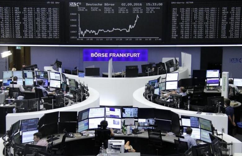 Traders work at their desks in front of the German share price index DAX board at the stock exchange in Frankfurt Germany