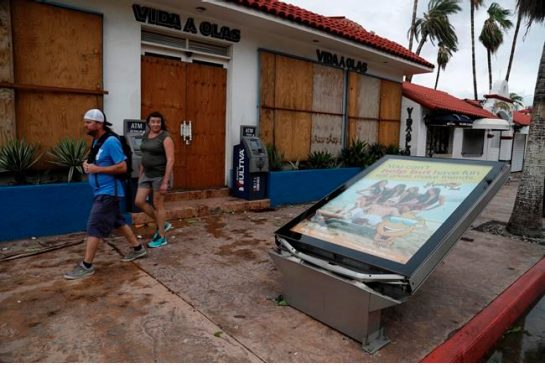 A couple walks next to an advertisement toppled by Hurricane Newton in Cabo San Lucas Mexico Tuesday Sept. 6 2016. Hurricane Newton shattered windows downed trees and knocked out power in parts of the twin resorts of Los Cabos on Tuesday but resident