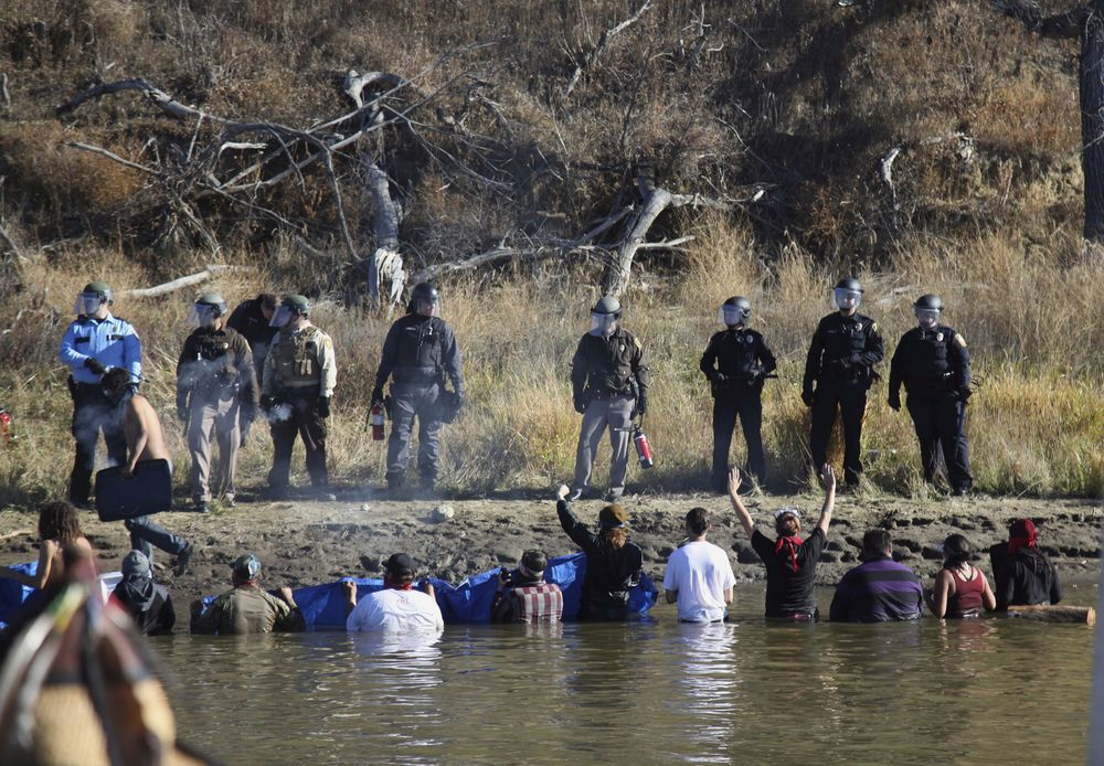 Dozens of protestors demonstrating against the expansion of the Dakota Access Pipeline wade in cold creek waters confronting local police as remnants of pepper spray waft over the crowd near Cannon Ball N.D. Wednesday Nov. 2 2016. Officers in riot