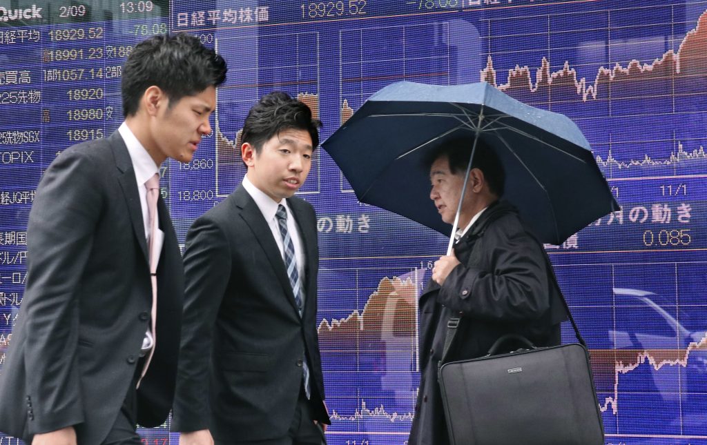 People walk past an electronic stock indicator of a securities firm in Tokyo Thursday