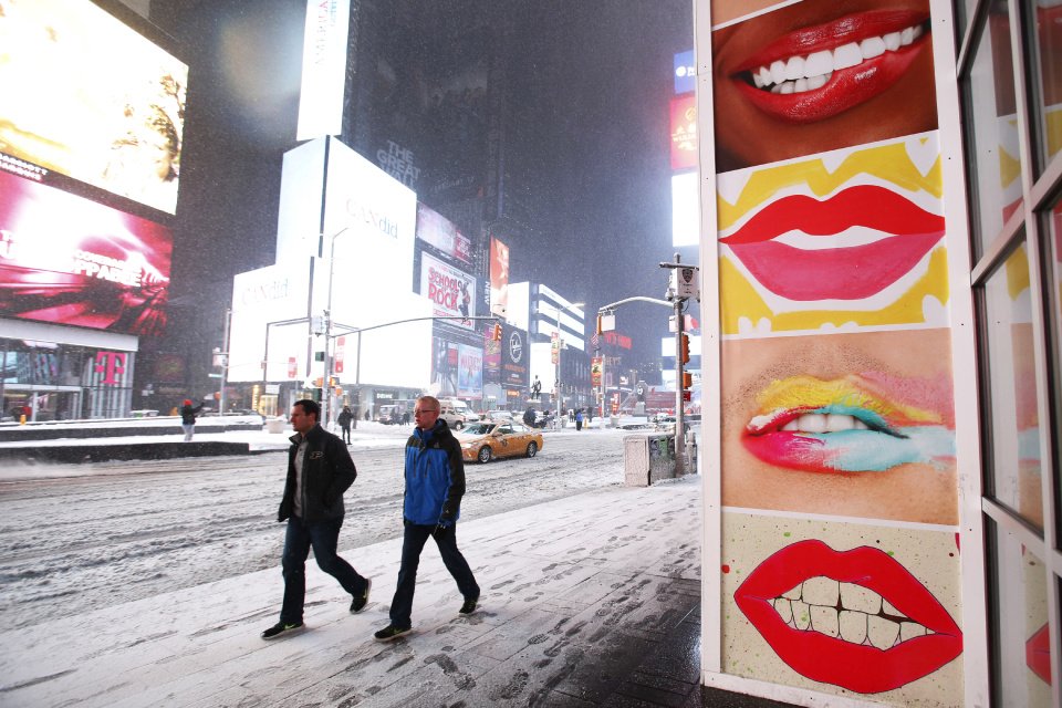 Caption + People walk through New York's Times Square during a snowstorm Tuesday