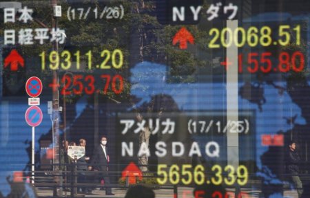 Pedestrians are reflected on an electronic board showing Japan's Nikkei average, the Dow Jones average and the stock averages of other countries outside a brokerage in Tokyo Japan