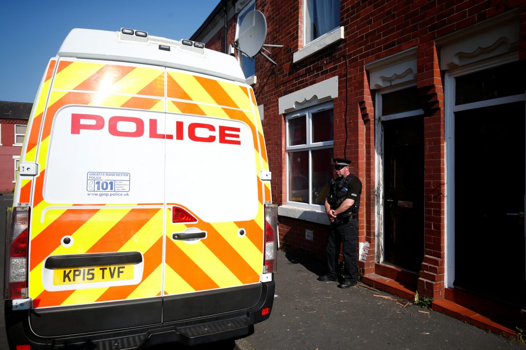 A police officer stand outside a property in Moss Side following overnight raids in Manchester Thursday