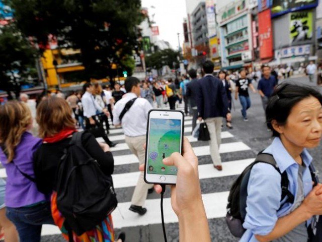 A man plays the augmented reality mobile game'Pokemon Go by Nintendo on his mobile phone as he walks at a busy crossing in Shibuya district in Tokyo Japan