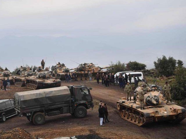 Villagers watch as Turkish army tanks and soldiers gather near the Syrian border