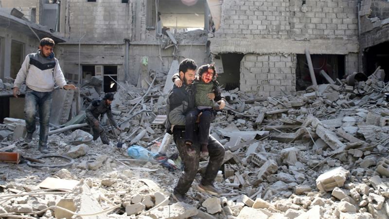 A man carries a wounded boy as he walks through damaged buildings in Eastern Ghouta on Wednesday