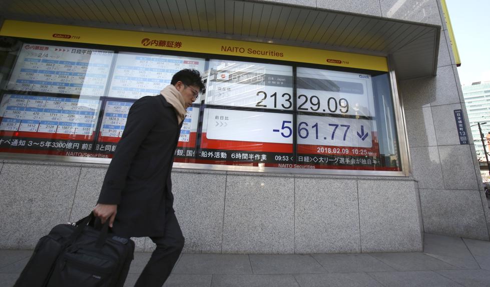 A man walks by an electronic stock board of a securities firm in Tokyo Friday Feb. 9 2018. Asian shares have opened lower and are tracking the overnight plunge on Wall Street. The Dow Jones industrial average plunged more than 1,000 points as a weeklon