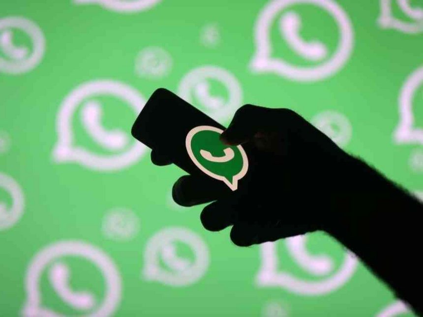 A man poses with a smartphone in front of displayed Whatsapp logo in this illustrati