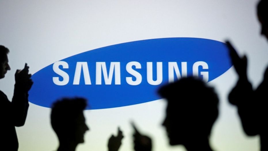 People are silhouetted as they pose with mobile devices in front of a screen projected with a Samsung logo in this